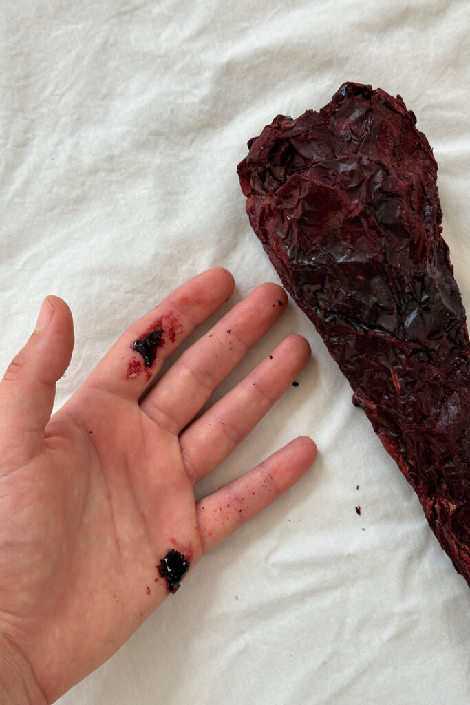 One year of menstrual blood harvested by Ashlee Zlatna and shaped into an icicle next to artist hand.